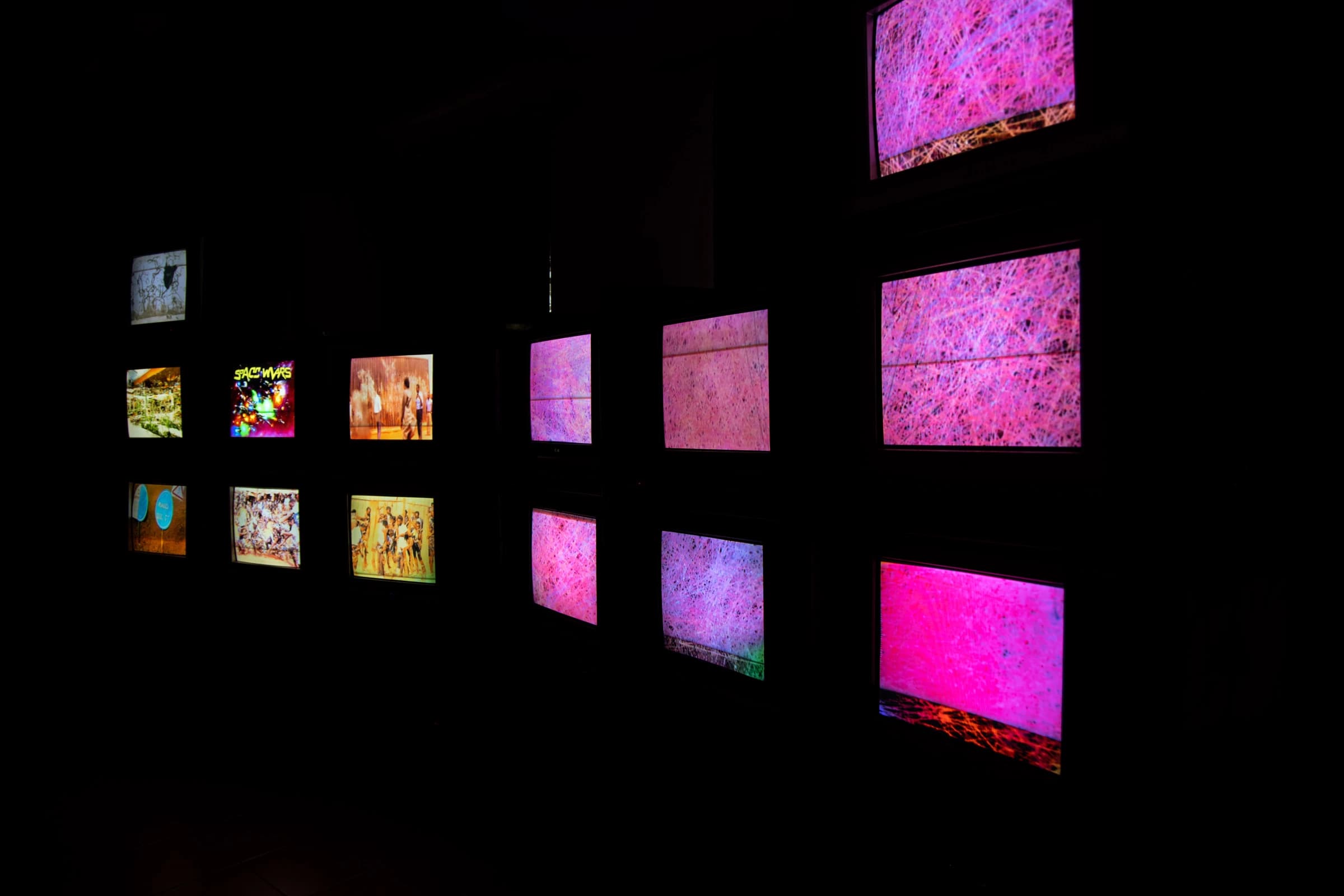 Colourful images illuminate a wall of CRT screens in a dark installation space