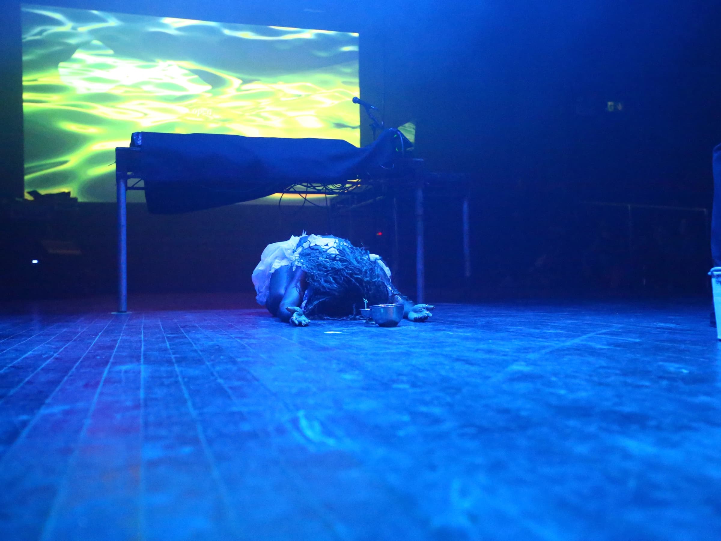A performer on a blue-lit stage beneath a projection of moving water